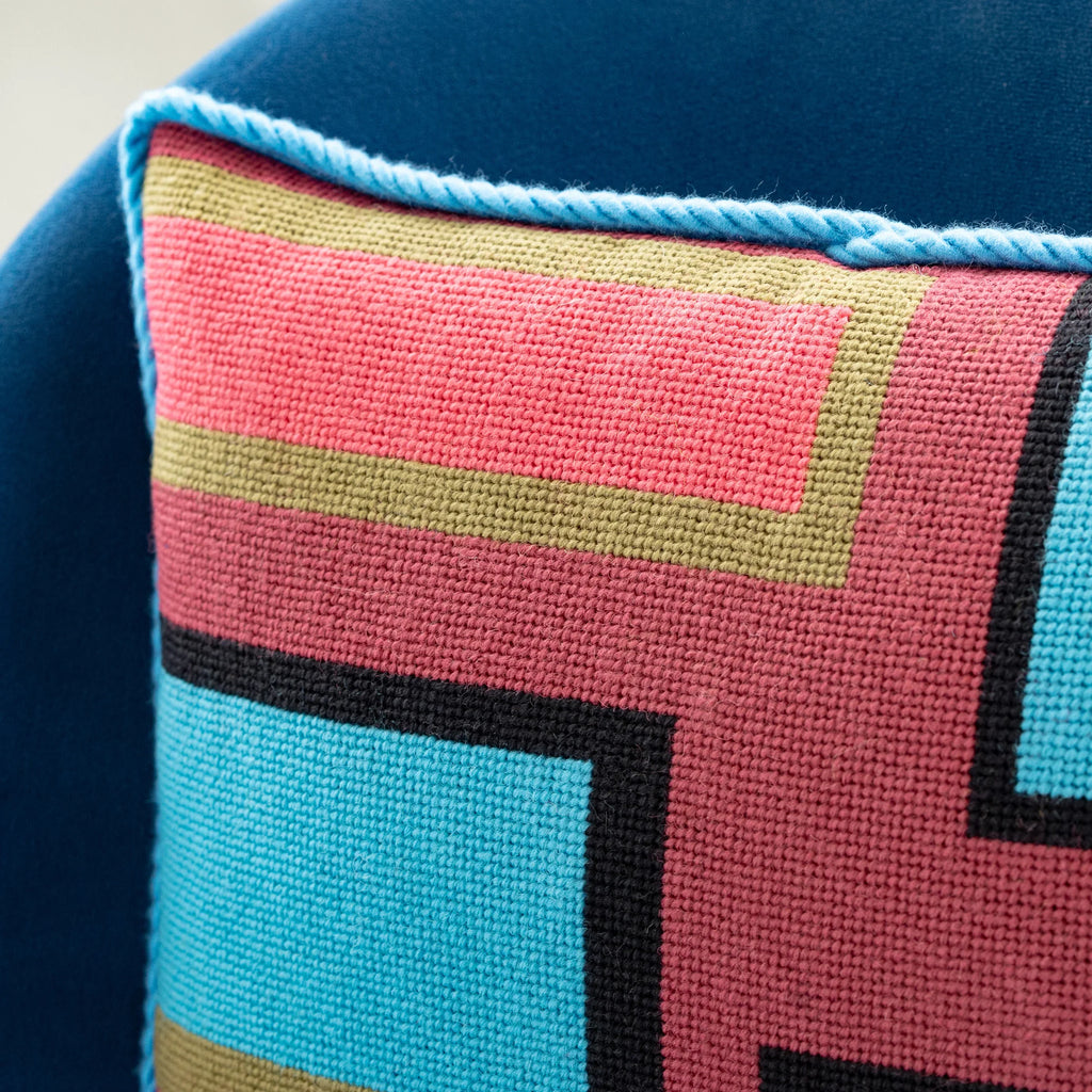 Detail of a colorful geometric patterned needlepointed cushion on a blue couch. Designed and sold by Daisy’s Needlepoint Kits.