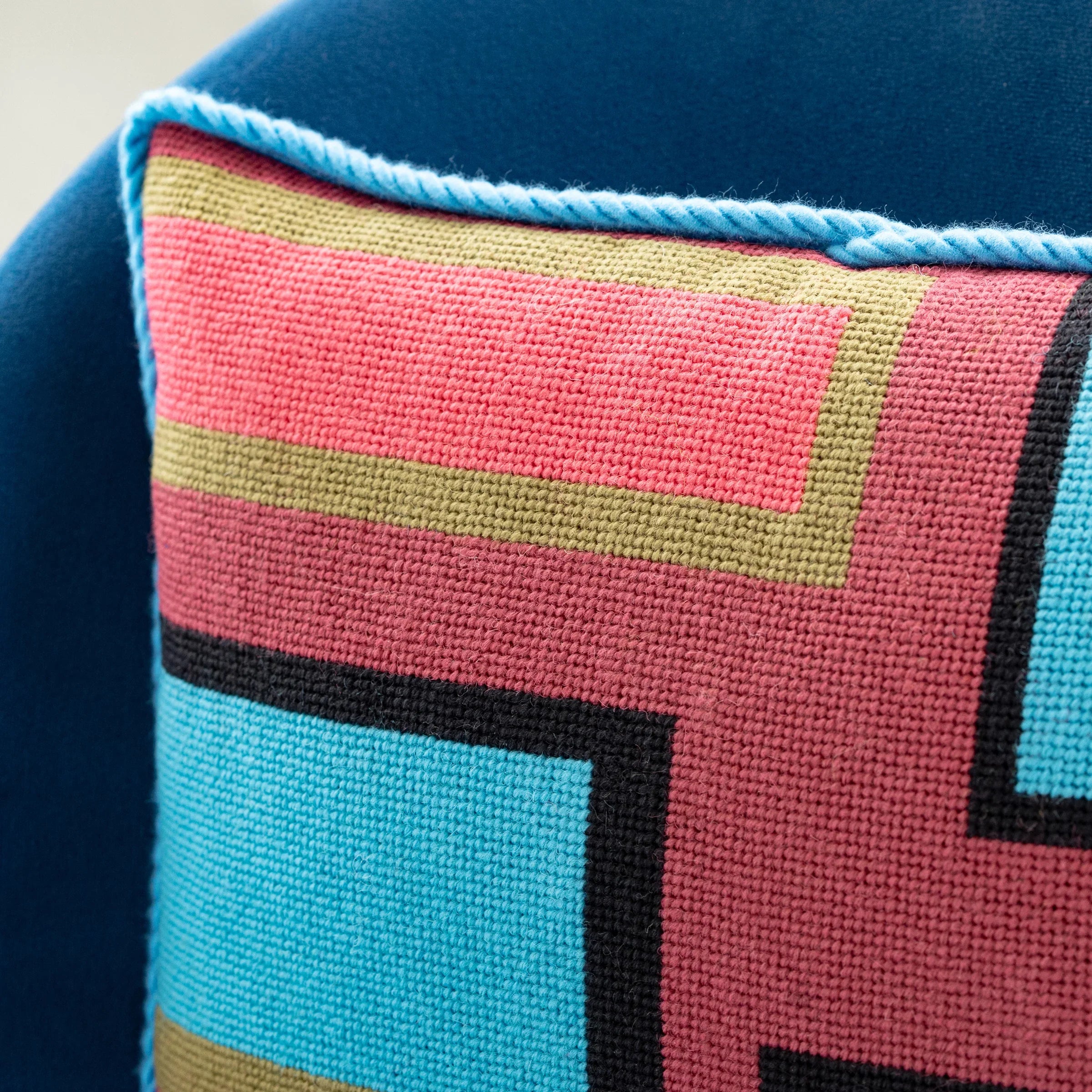 Detail of a colorful geometric patterned needlepointed cushion on a blue couch. Designed and sold by Daisy’s Needlepoint Kits.