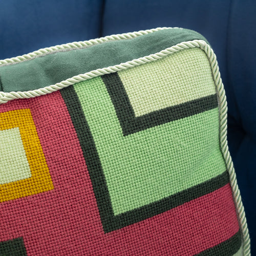 Detail of a colorful geometric patterned needlepointed cushion on a blue couch. Designed and sold by Daisy’s Needlepoint Kits.