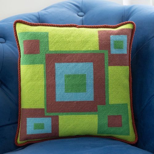 Colorful geometric-patterned needlepointed pillow on a blue couch