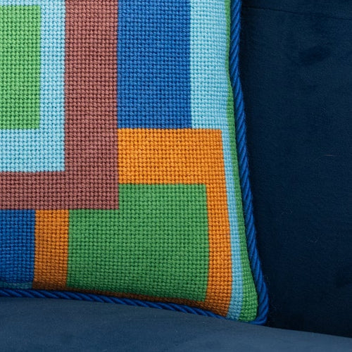 Detail of a colorful geometric patterned needlepointed cushion on a blue couch. Designed and sold by Daisy’s Needlepoint Kits.