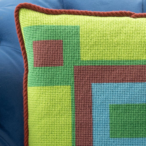 Detail of a colorful geometric patterned needlepointed cushion on a blue couch.
