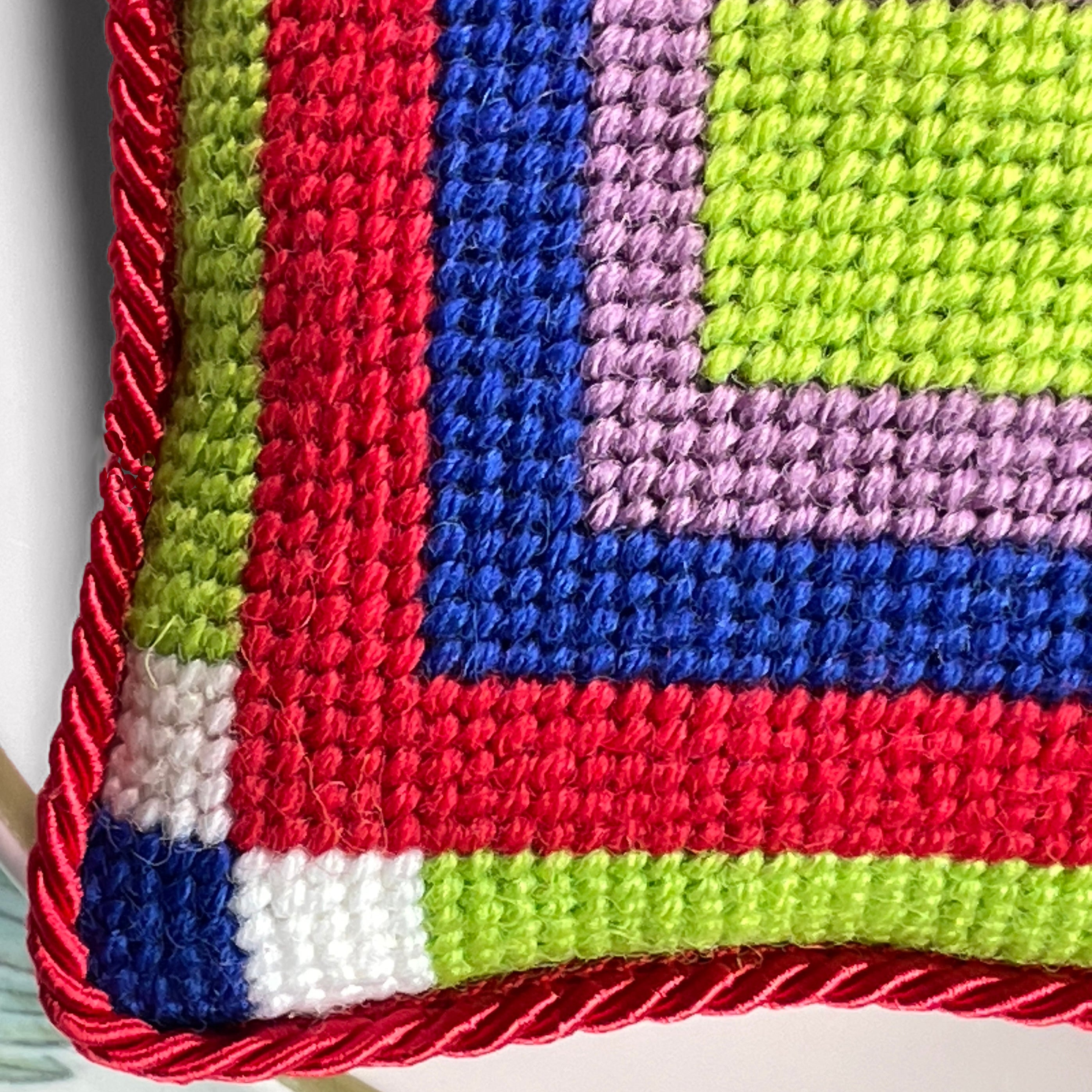 Detail of a colorful geometric patterned needlepointed cushion on a blue couch. Designed and sold by Daisy’s Needlepoint Kits.