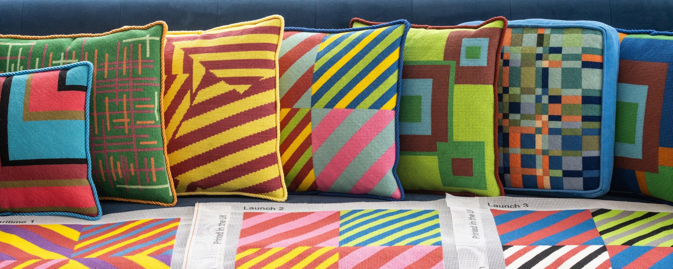 Colorful geometric-patterned pillows on a sofa. Designs by Daisy's Needlepoint Kits.